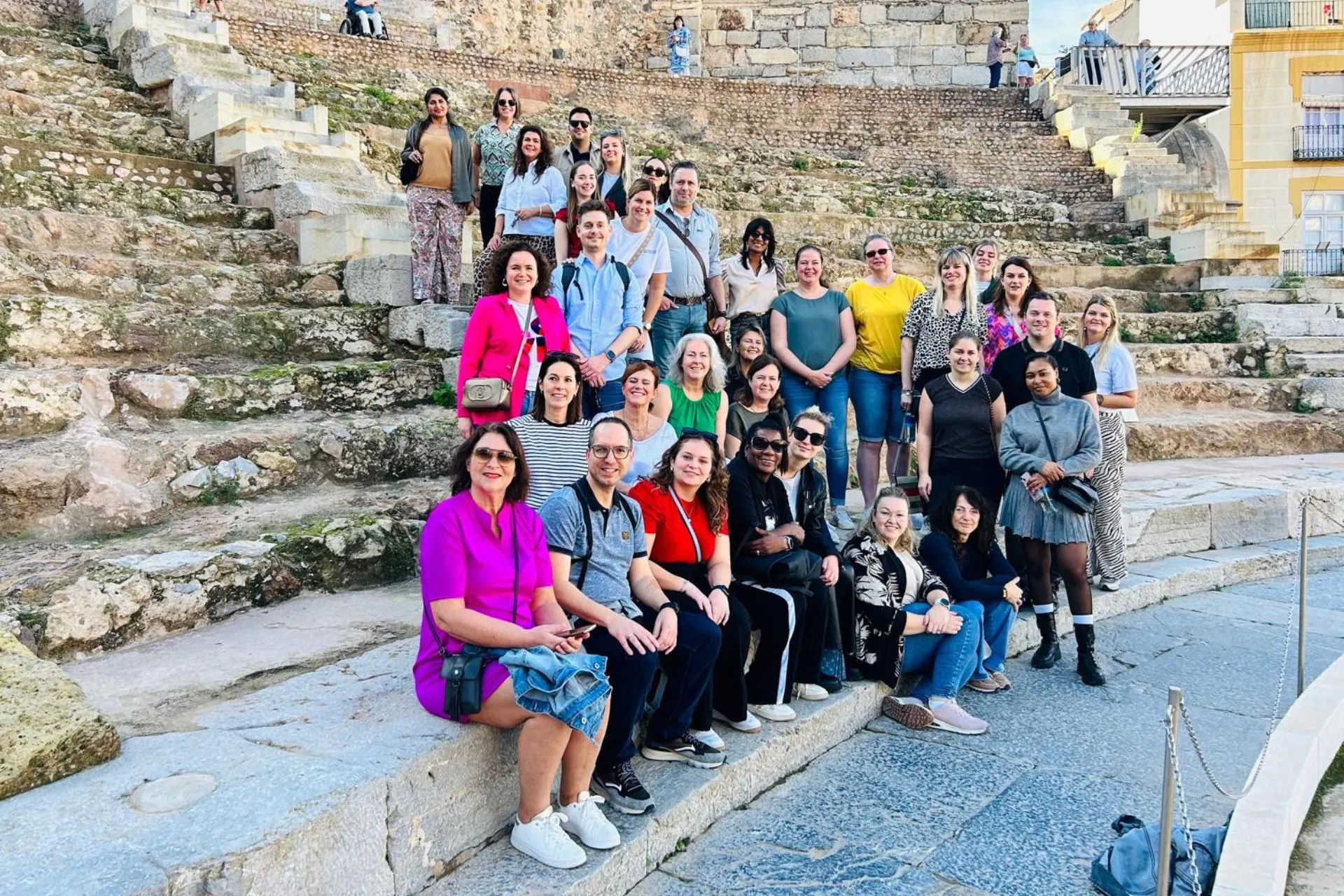 Groepsfoto van reizigers die poseren in een historische arena in Cartagena, Spanje, omringd door stenen trappen