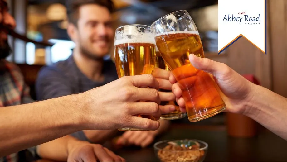 Drie vrienden proosten met bier in het bruine café Abbey Road, lachend en genietend van elkaars gezelschap.