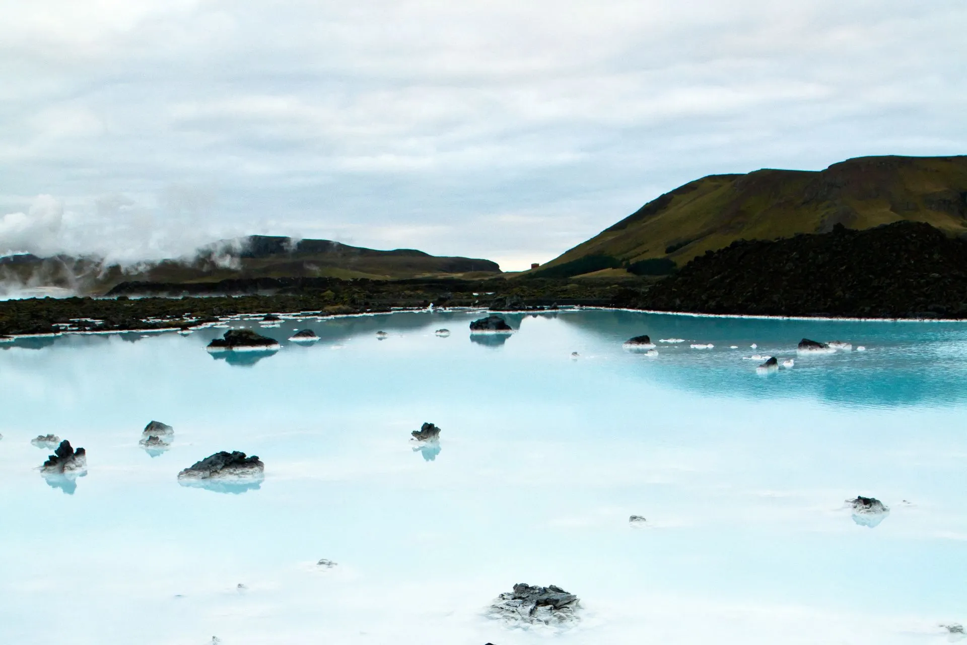 Rustig landschap van de Blue Lagoon in IJsland, met blauw geothermisch water, zwarte lavarotsen en een heuvelachtig landschap op de achtergrond.
