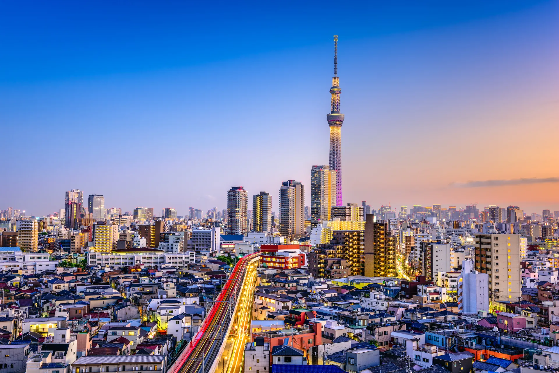 De skyline van Tokio tijdens de zonsondergang, met de stad die baadt in warme oranje en paarse tinten, terwijl de iconische torens en wolkenkrabbers zich aftekenen tegen de kleurrijke lucht.