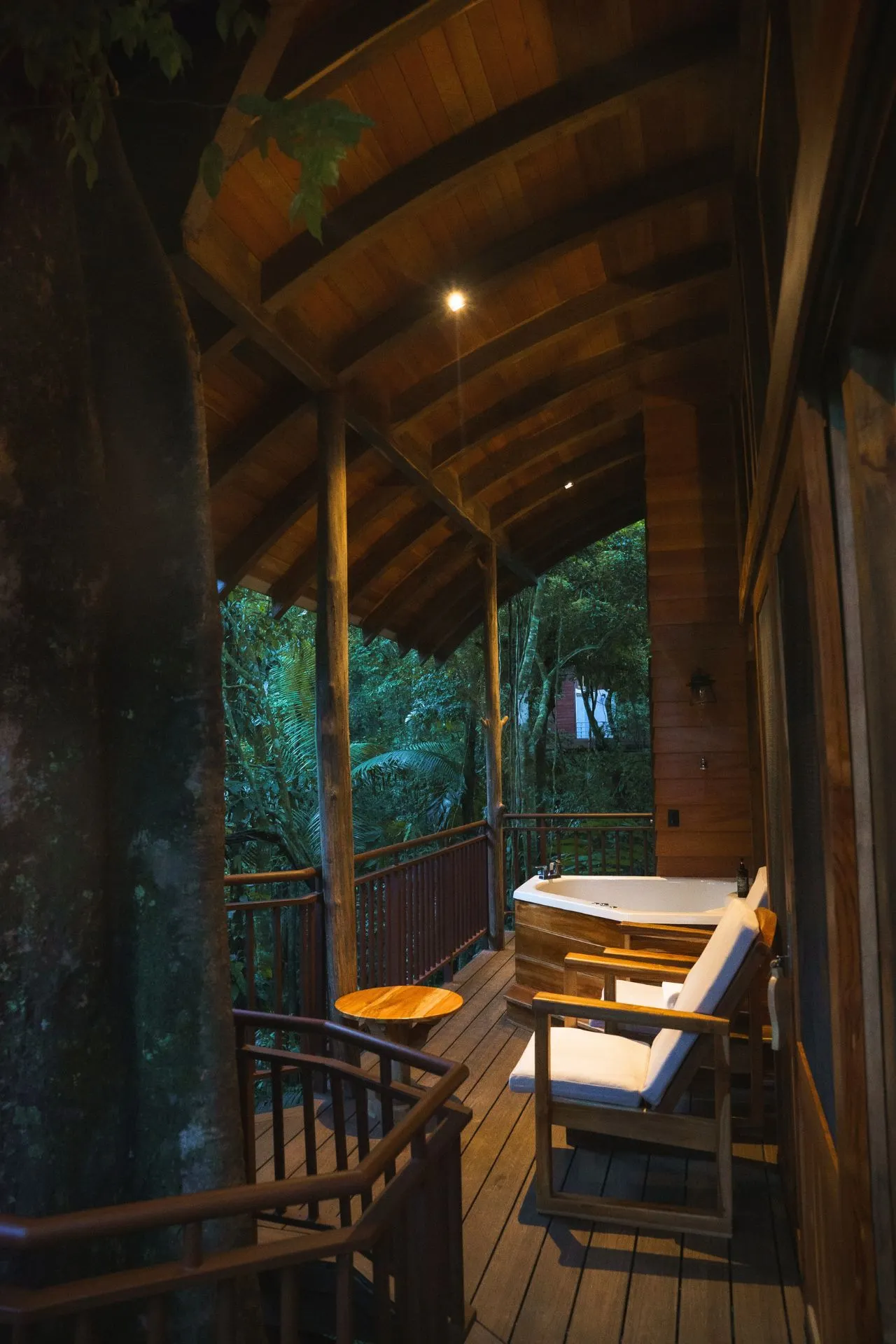 Houten veranda met een bubbelbad en comfortabele stoelen, omgeven door de jungle.