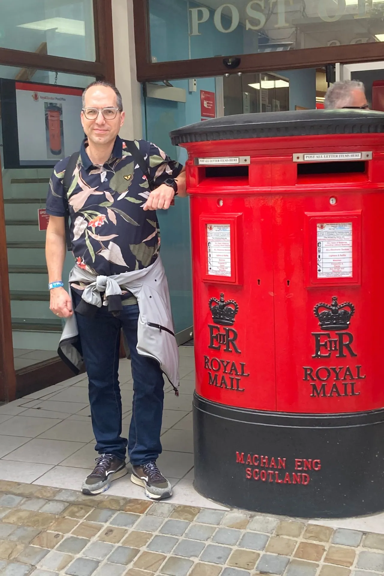 Reisadviseur Dino poserend naast een rode brievenbus van Royal Mail met een Post Office gebouw op de achtergrond in Gibralta