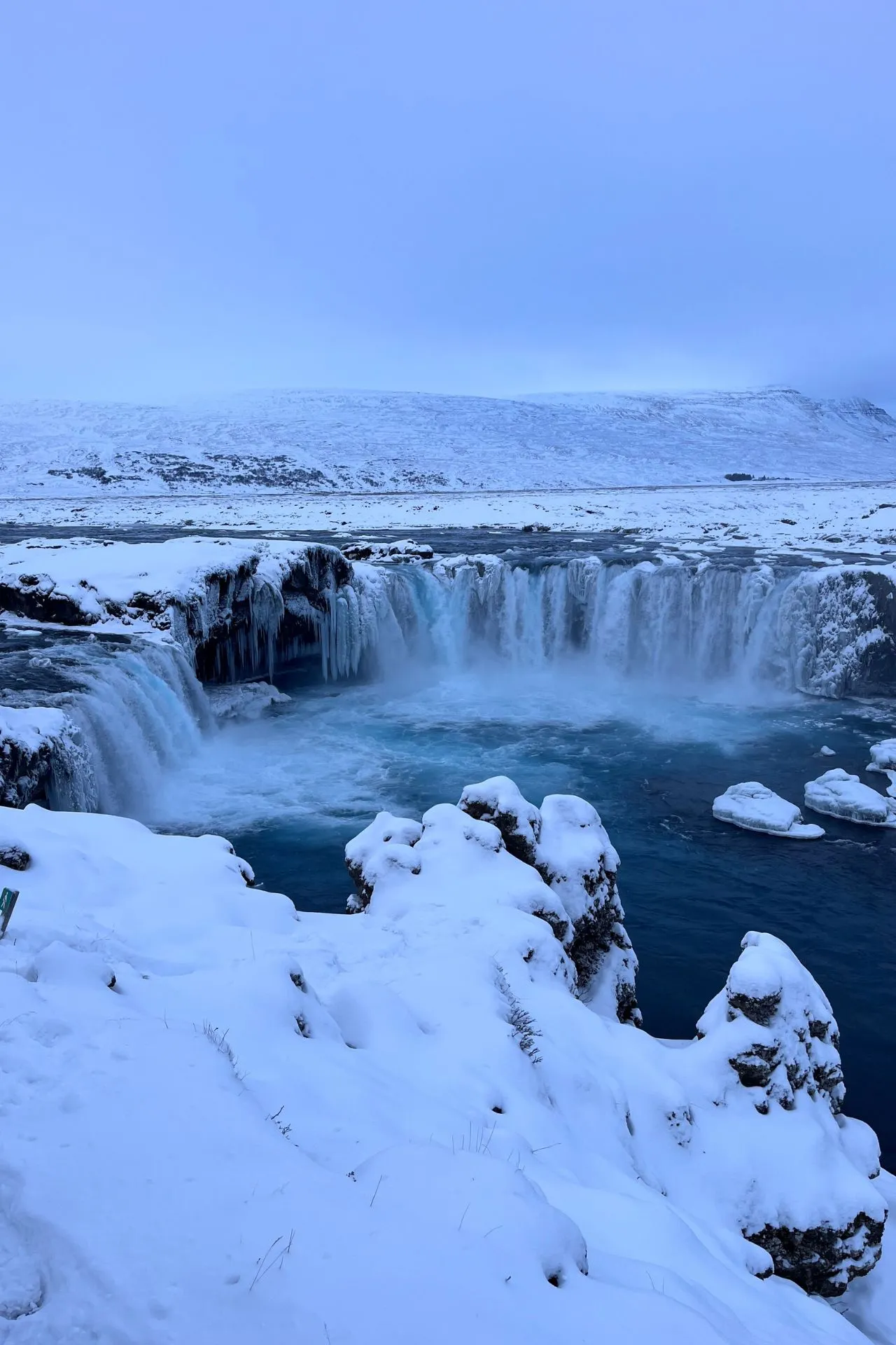 De bevroren Godafoss‑waterval omringd door sneeuw en ijs in de winter.
