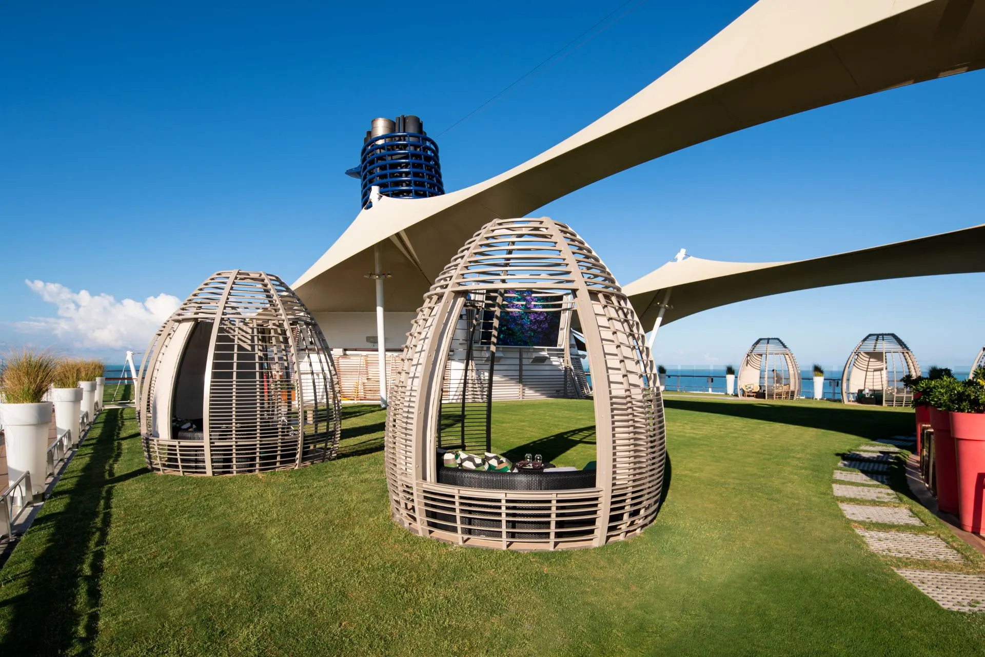 Buitenlounge aan boord van een Celebrity Cruises schip met moderne cabana’s en groene ontspanningsruimte, passend bij de luxe cruise-ervaring.
