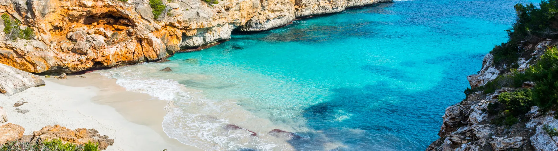 Luchtfoto van het zandstrand van Mallorca met helderblauw water, omringd door rotsen.