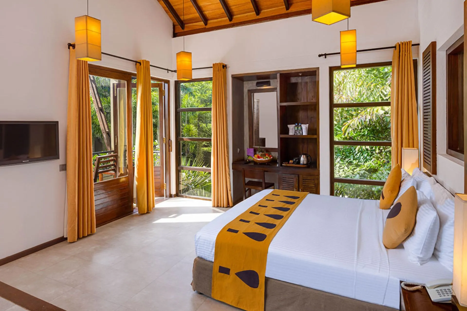 Ruime en sfeervolle kamer bij Chaarya Resort & Spa Yala met houten dakconstructie, warme verlichting, groot tweepersoonsbed en openslaande deuren naar een groene tuin.