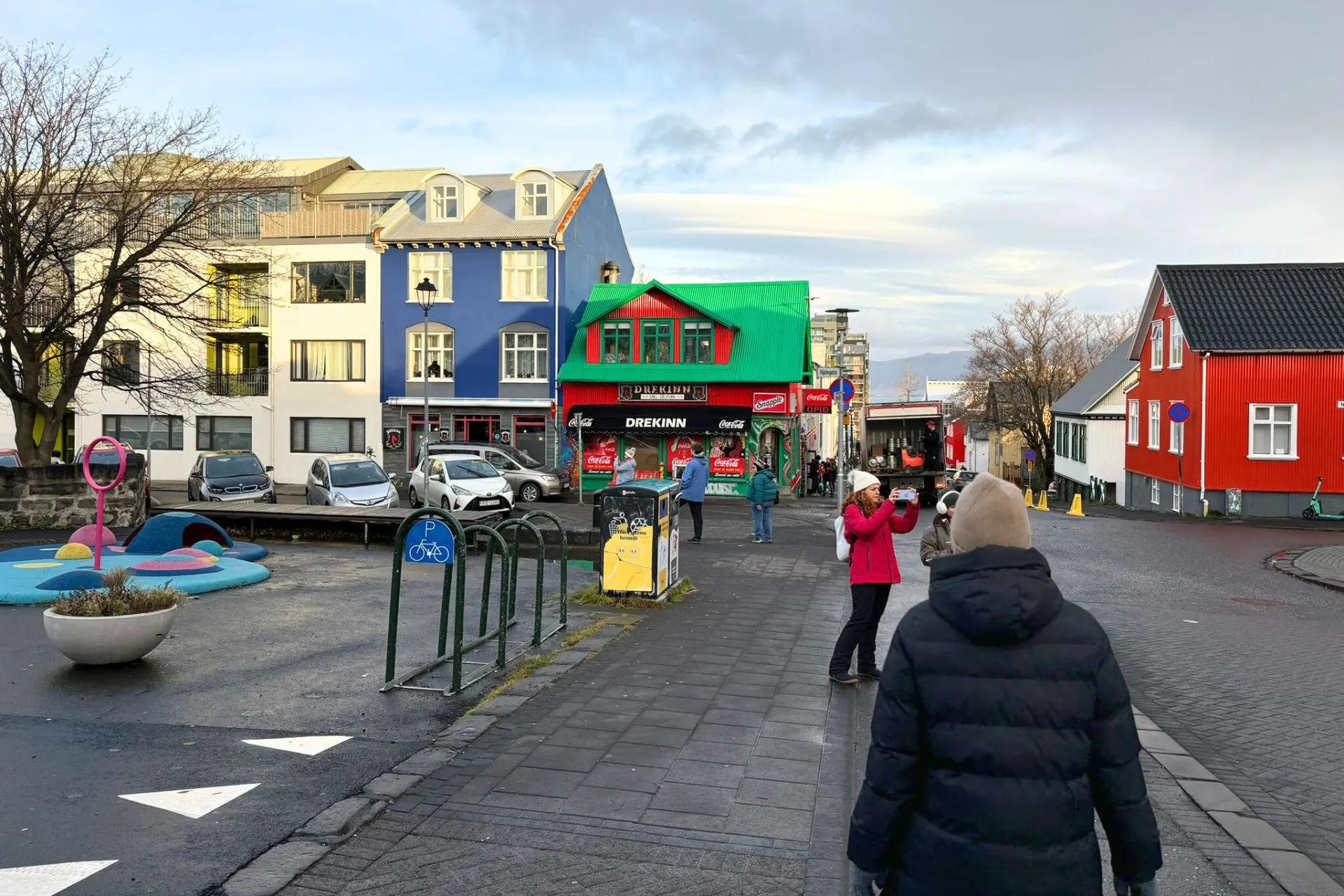 Straatbeeld in Reykjavik met felgekleurde huizen, enkele mensen die wandelen en een speelse openbare ruimte met een kunstwerk op de voorgrond.