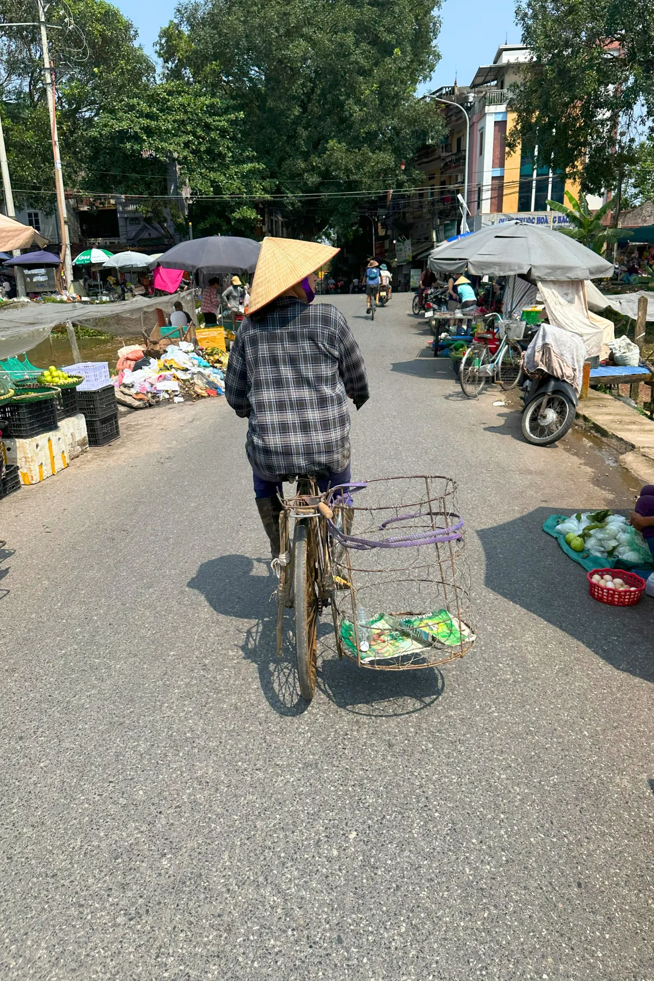 Vietnamese man op een fiets, rijdend door een druk marktstraatje vol kleuren en bedrijvigheid.
