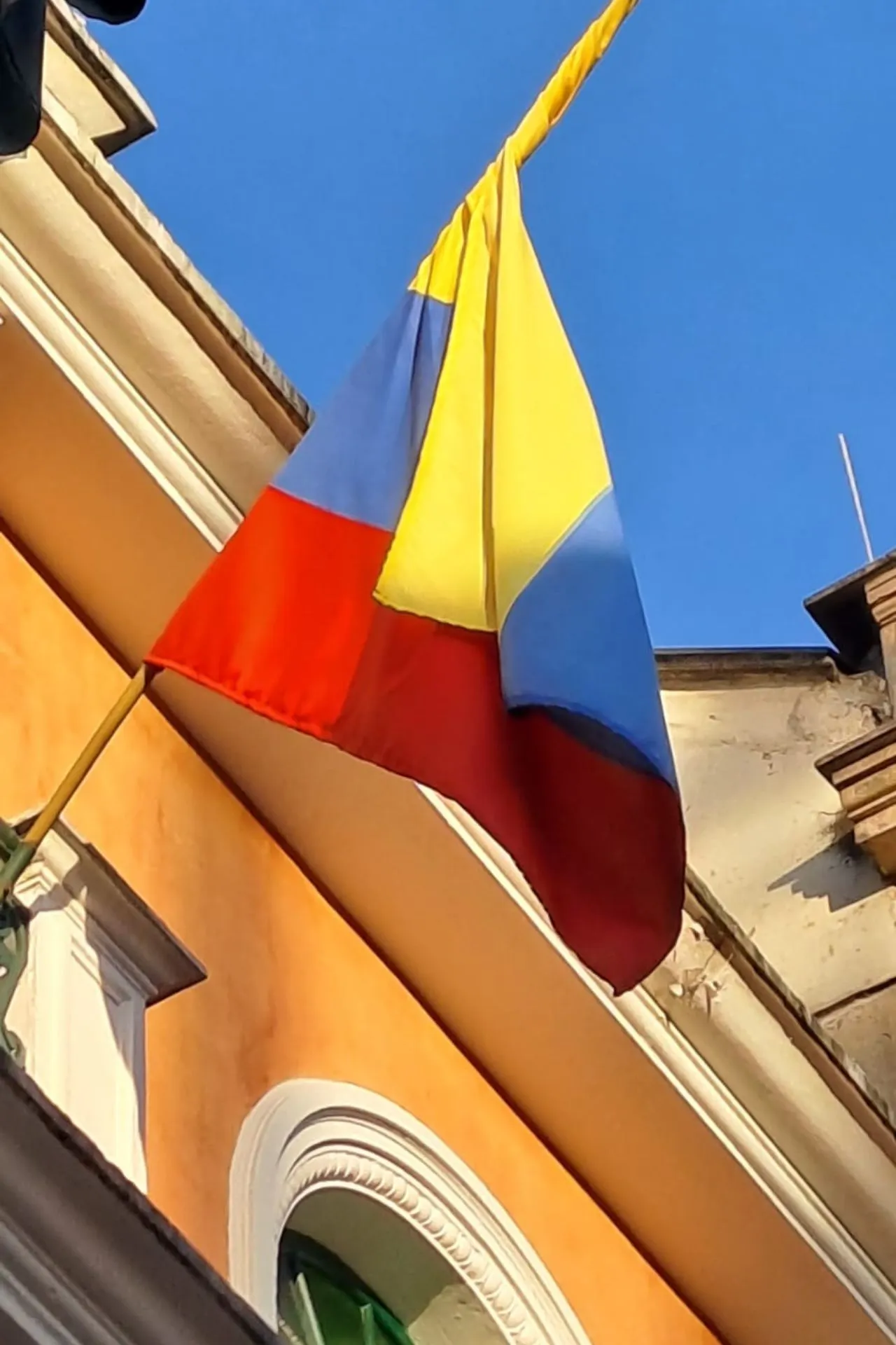 Colombiaanse vlag met horizontale banen in geel, blauw en rood, wapperend aan een gebouw tegen een heldere blauwe lucht.