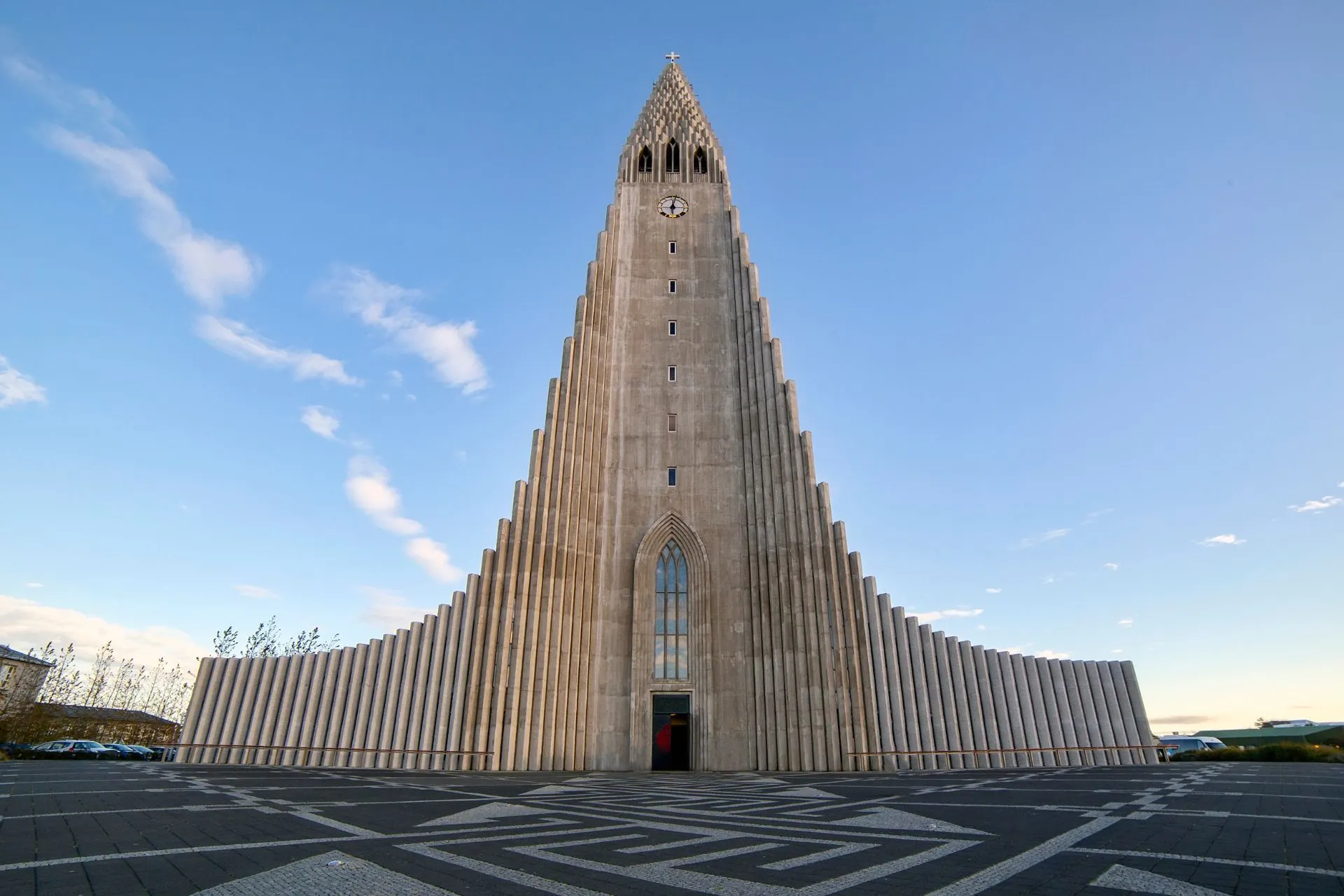 Vooraanzicht van de iconische Hallgrímskirkja in Reykjavik, een moderne betonnen kerk met geometrisch ontwerp en een blauwe lucht erboven.