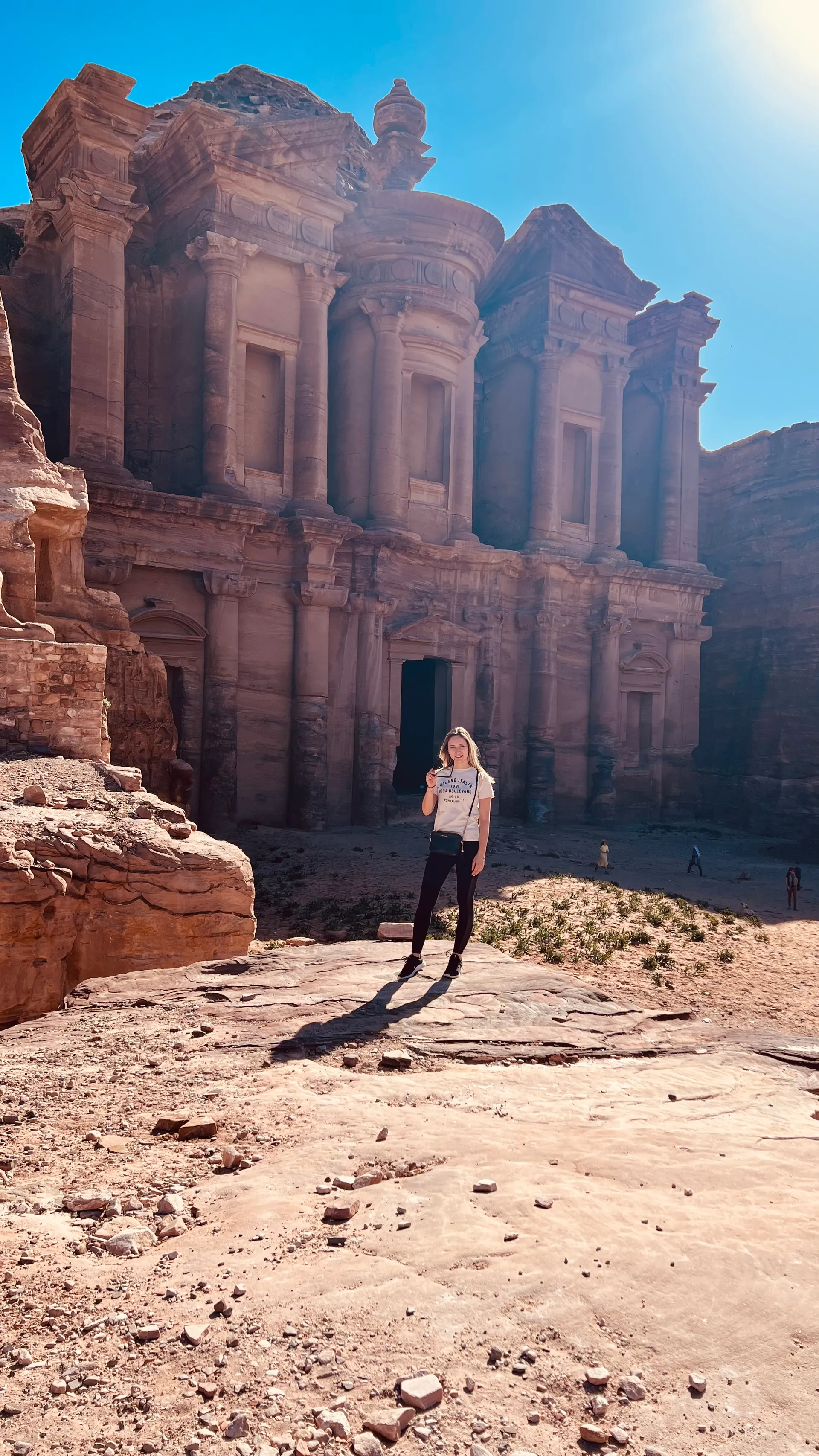 Emmie staat in Petra, Jordanië, met de indrukwekkende rotsformaties en oude architectuur van de stad op de achtergrond.