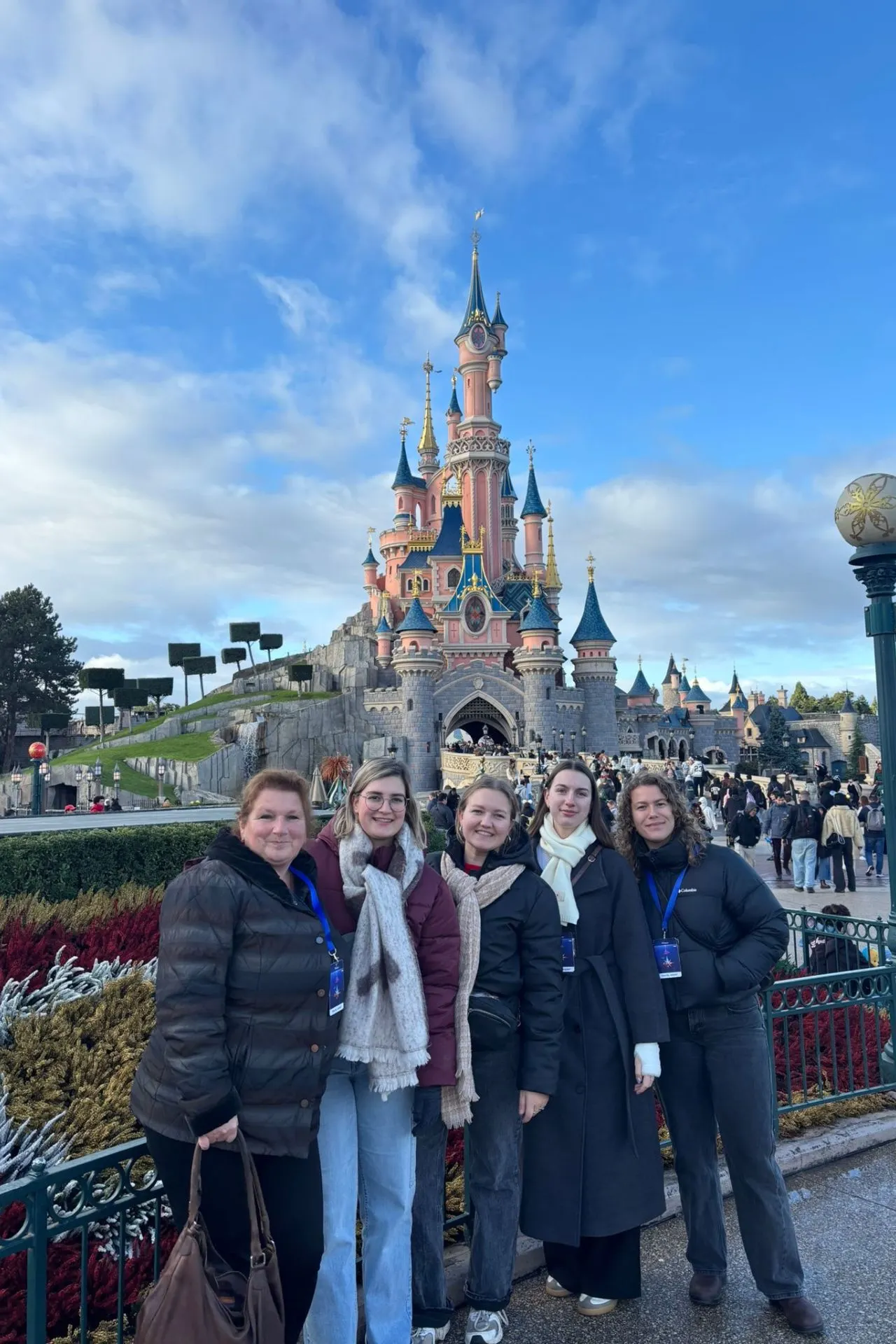 Een groep vriendinnen poseert lachend voor het iconische Kasteel van Doornroosje in Disneyland Parijs. Ze staan op het kleurrijke plein van Disneyland Park, omringd door bloemen en bezoekers. De blauwe lucht en het sprookjesachtige kasteel creëren echte Disney-magie. De foto straalt plezier, vakantiegevoel en een dag vol attracties, parades en avontuur in het populaire pretpark Disneyland Parijs uit.
