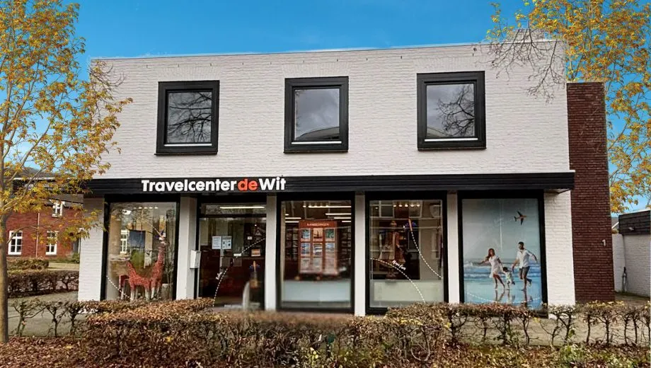 Filiaal Heesch van Travelcenter de Wit, met een mooie blauwe lucht en bomen en struiken.