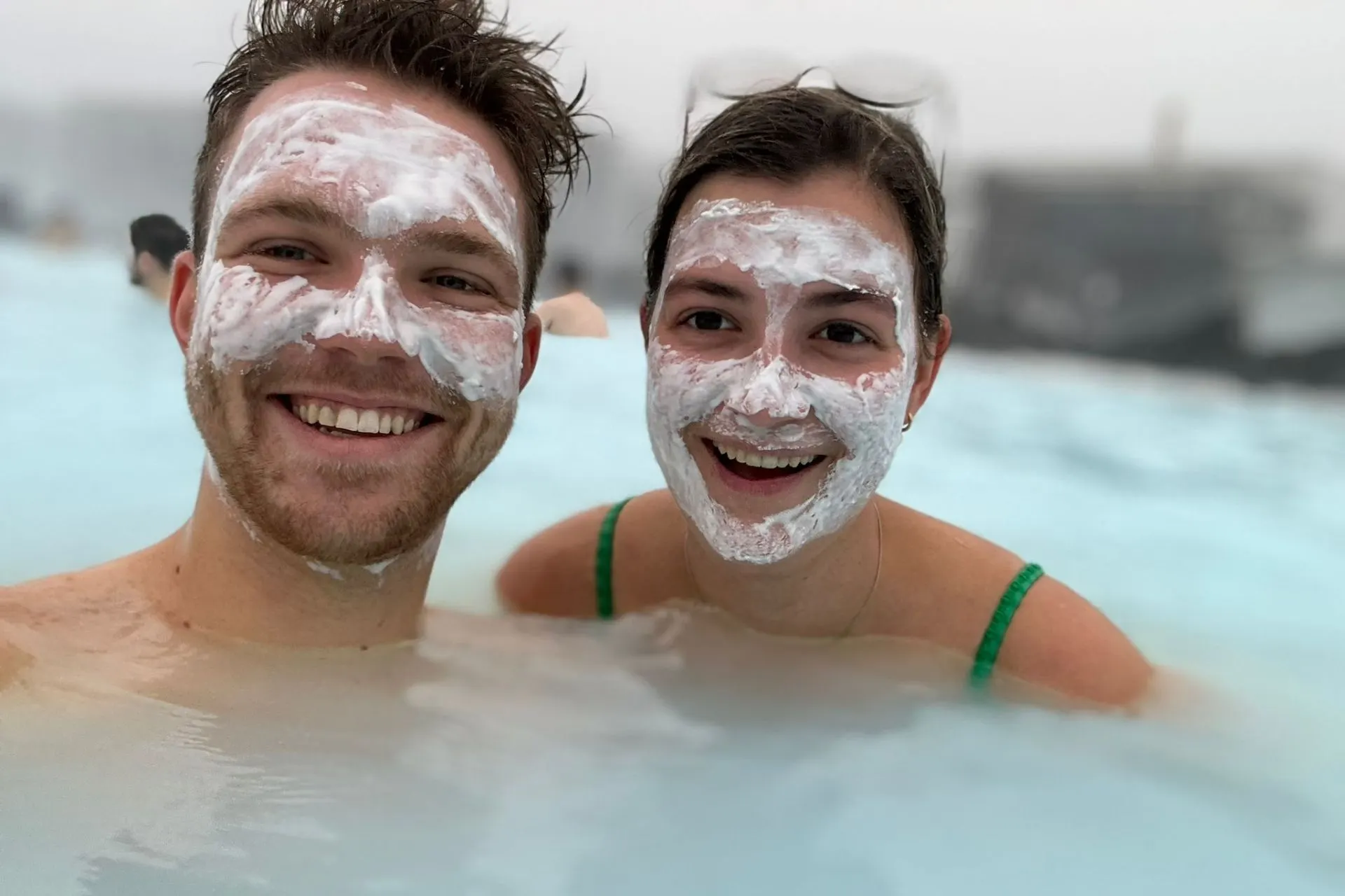 Reisadviseur Vera en haar vriend met witte moddermaskers geniet van het warme water in de Blue Lagoon in IJsland, met een mistige achtergrond.