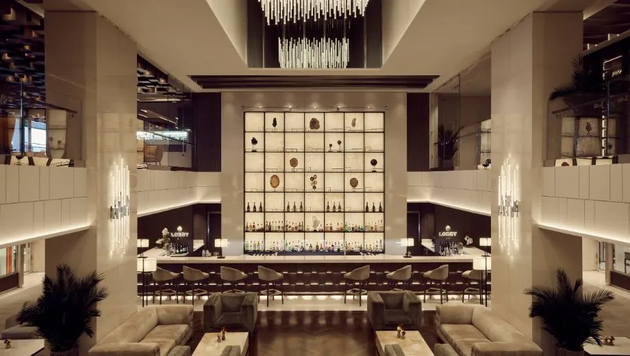 Luxe bar en lounge aan boord van een Explora Cruise schip, met een indrukwekkend hoog plafond, moderne verlichting en een elegante opstelling van flessen achter een verlichte wand. Deze ruimte straalt exclusiviteit en comfort uit, ideaal voor gasten die genieten van premium cocktails en ontspannen in een stijlvolle omgeving. Ontdek waarom Explora Journeys bekendstaat om zijn verfijnde design, hoogwaardige service en ultieme cruise-ervaring naar unieke bestemmingen.