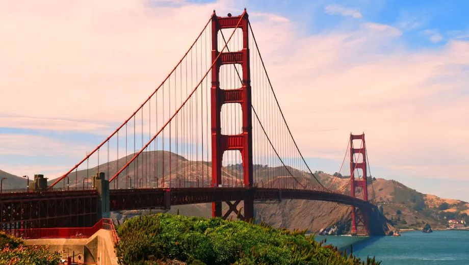 Golden Gate Bridge met rood-oranje torens, blauwe en roze lucht, en groene heuvels – iconisch uitzicht op San Francisco.