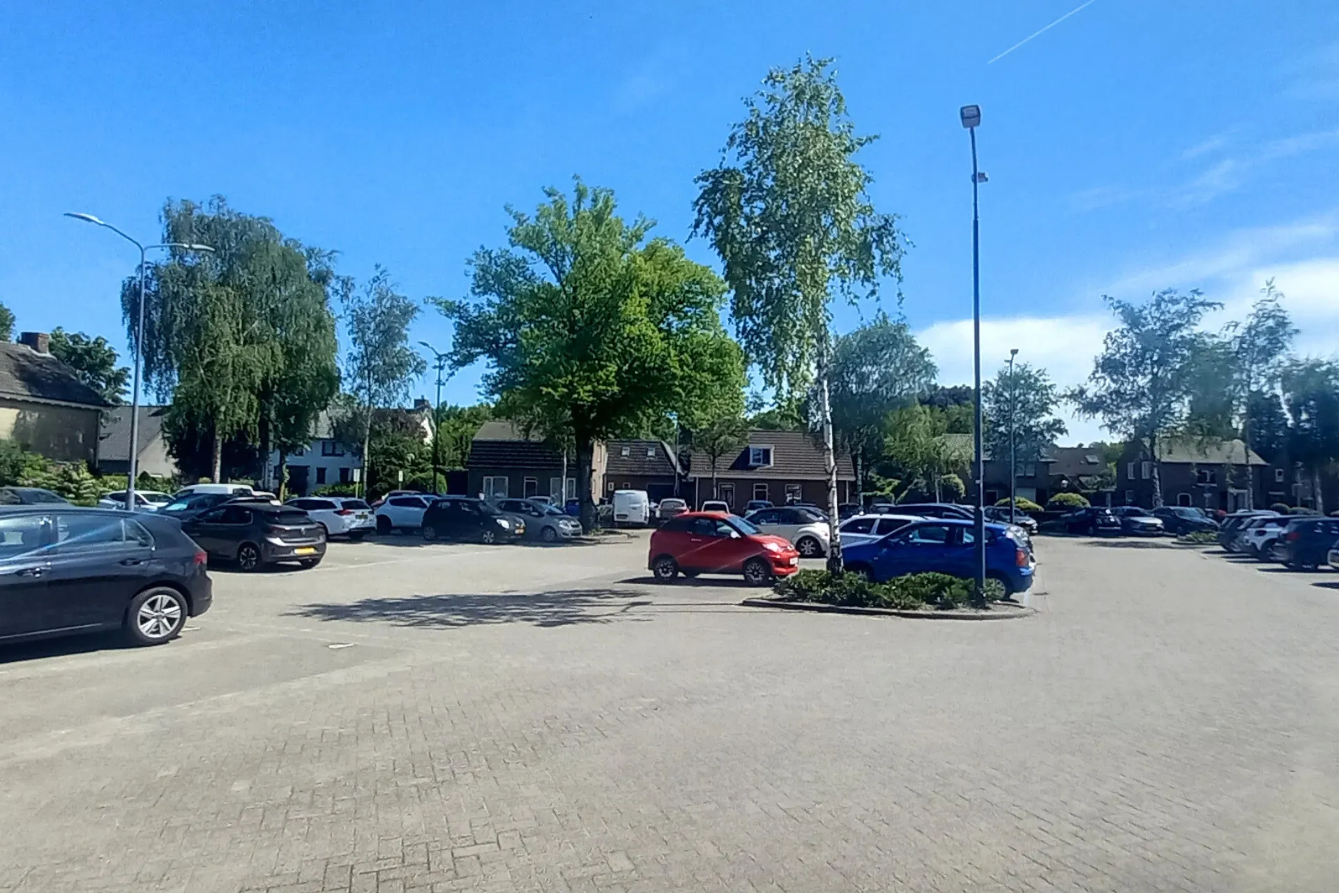 Parkeerplaats achter gemeenschapshuis De Kentering in Rosmalen, met geparkeerde auto's en omringend groen.