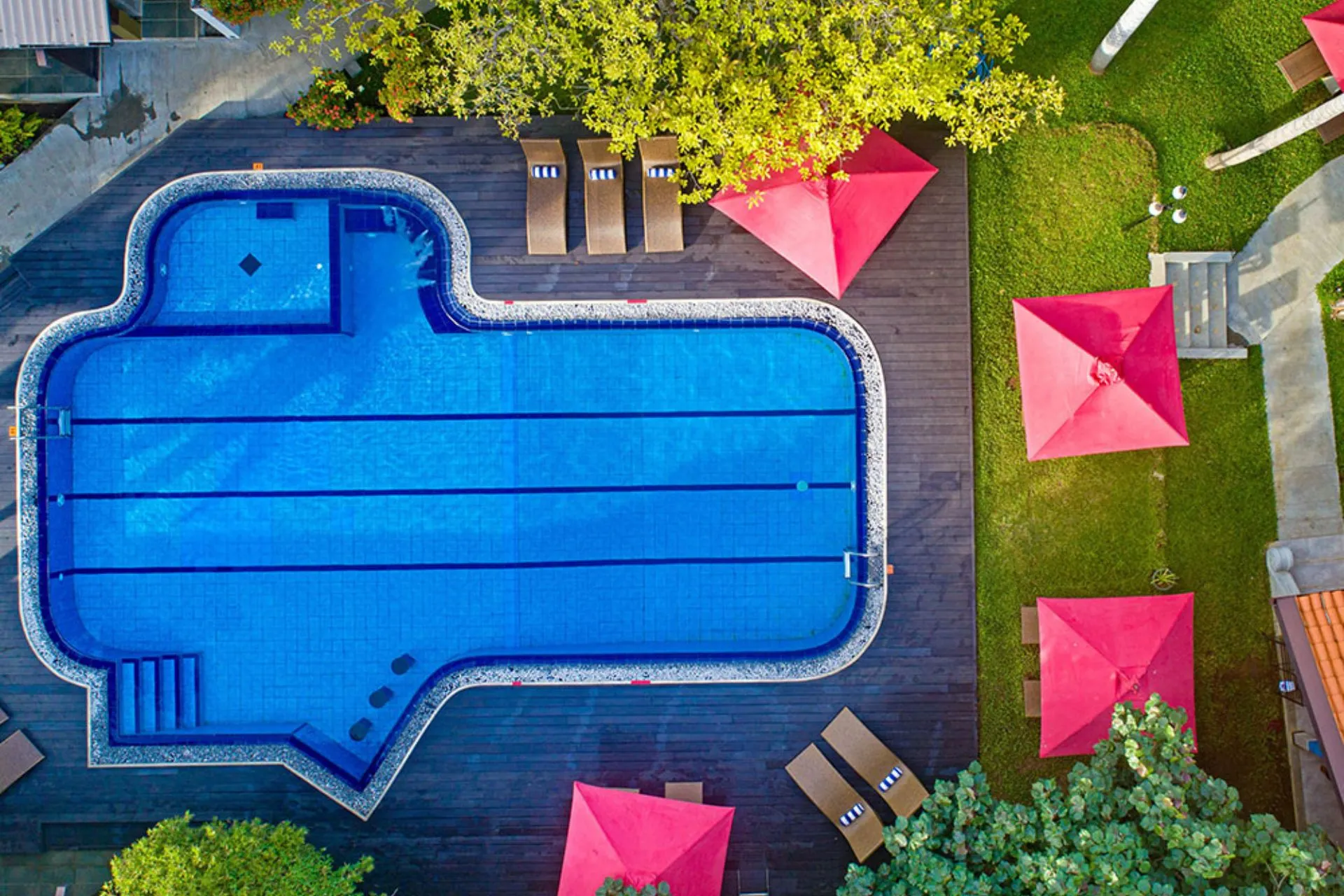 Bovenaanzicht van het zwembad van Chaarya Resort & Spa Yala, omgeven door houten terrassen, ligbedden en felrode parasols in een tropische tuinsetting.