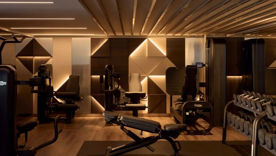 Moderne fitnessruimte aan boord van een Explora Cruise schip, uitgerust met professionele fitnessapparatuur, gewichten en een stijlvol interieur met warme verlichting en geometrische wandpanelen. Deze foto benadrukt de wellness- en sportfaciliteiten die Explora Journeys biedt voor een luxe cruisevakantie. Geniet van gezondheid, ontspanning en premium service op zee, ideaal voor reizigers die comfort en fitness willen combineren tijdens hun exclusieve cruise-ervaring.