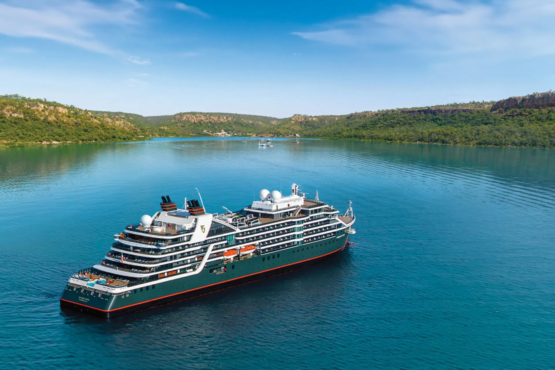 Het expeditieschip ms Hanseatic Inspiration van Holland America Line dobbert in turquoise water voor de kust van Australië, omringd door groene heuvels.
