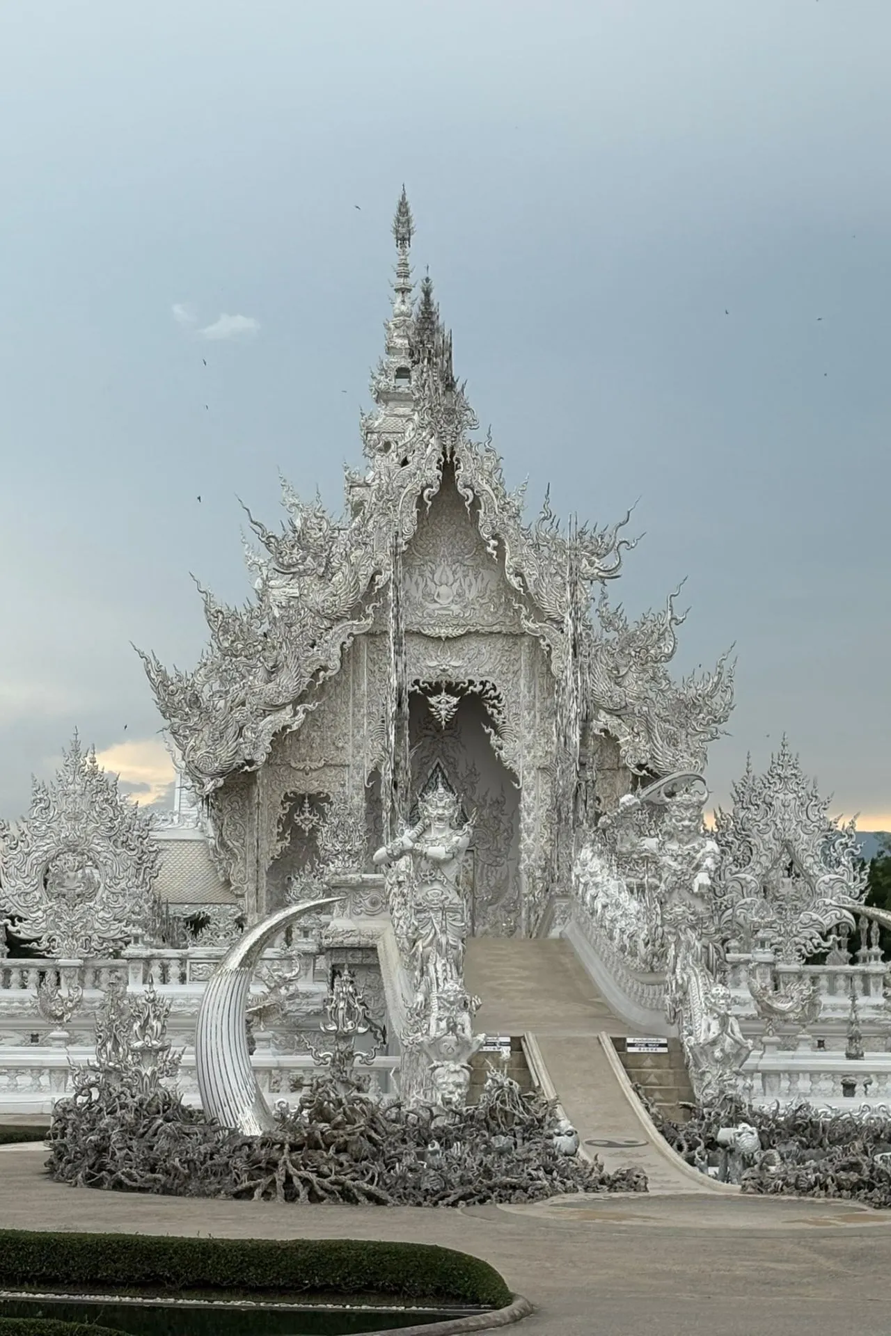 Prachtig gedetailleerde witte tempel (Wat Rong Khun) in Chiang Rai, Thailand, met sierlijke versieringen en ingewikkelde patronen tegen een bewolkte lucht.