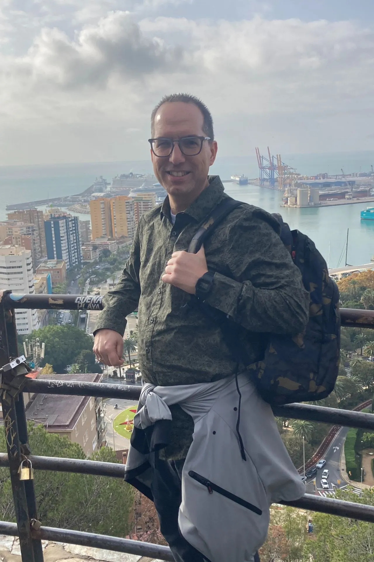 Reisadviseur Dino poseert op een balkon met uitzicht over de haven van Malaga, met cruiseschepen en gebouwen op de achtergrond