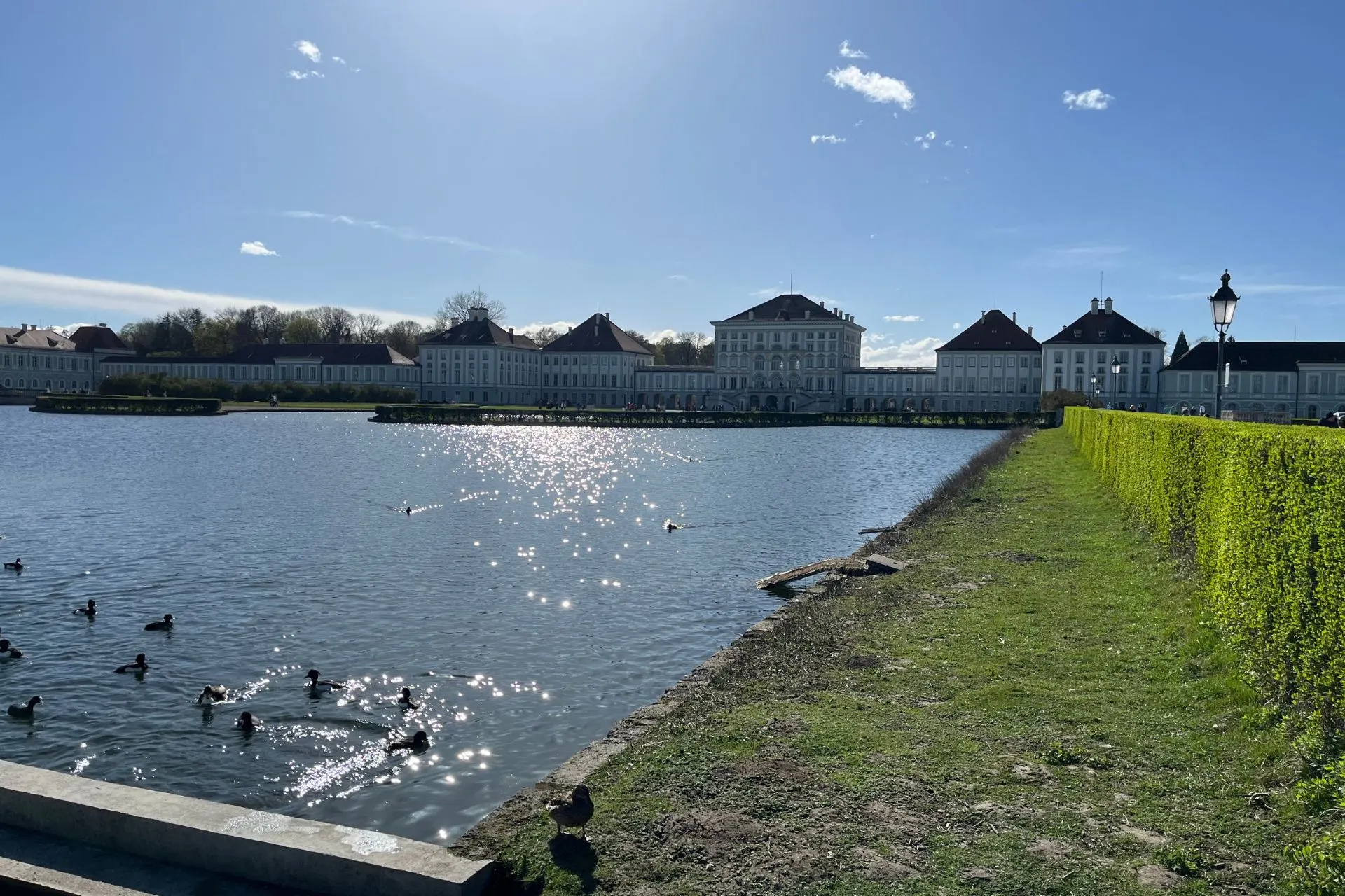 Het majestueuze Schloss Nymphenburg in München, met een schitterend reflecterend meer en een idyllisch groen park op de voorgrond.