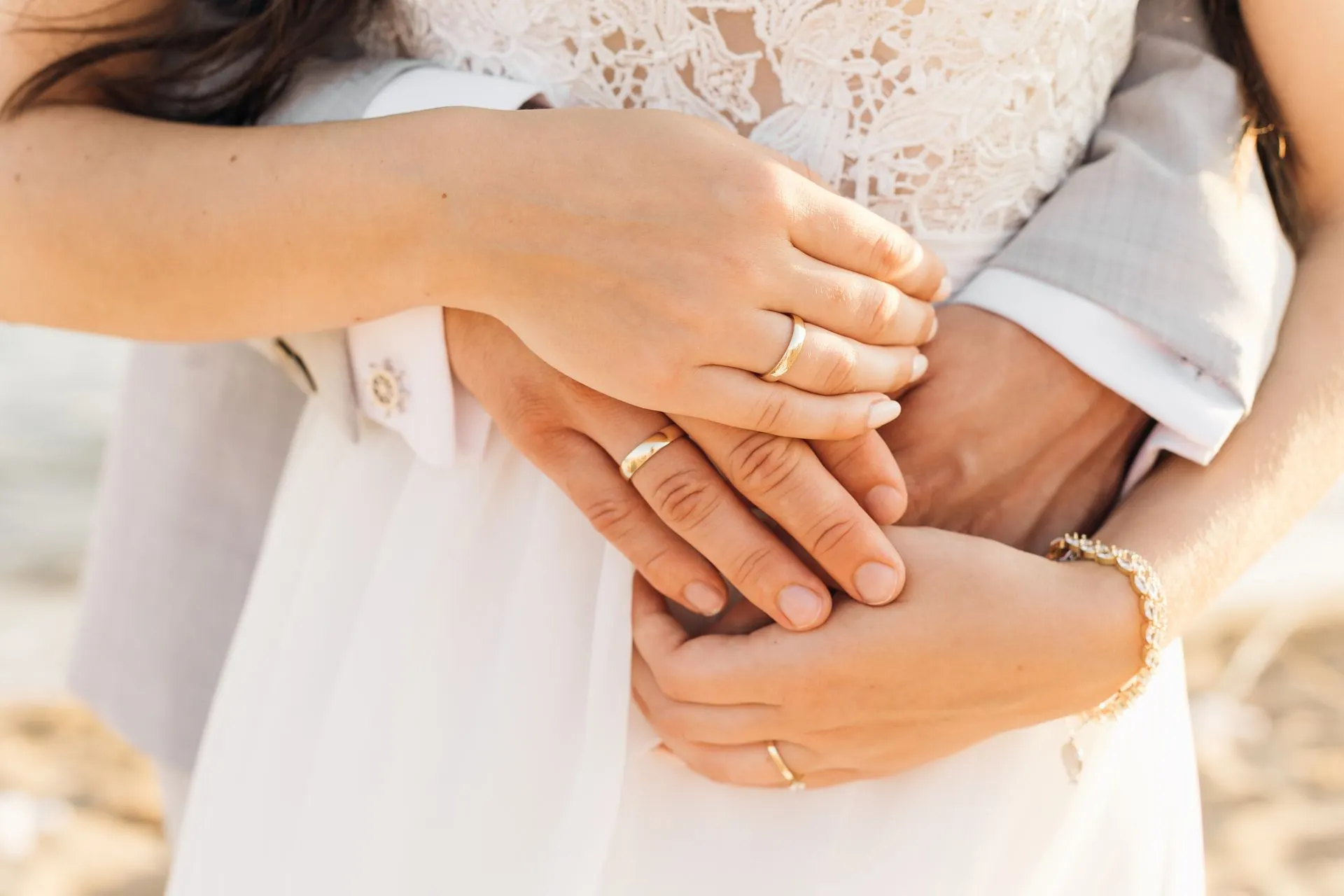 De handen van een man zijn voorzichtig over die van zijn pasgetrouwde vrouw gevouwen, hun ringen schitteren in het zachte licht. Een moment van liefde en verbondenheid na hun huwelijk.