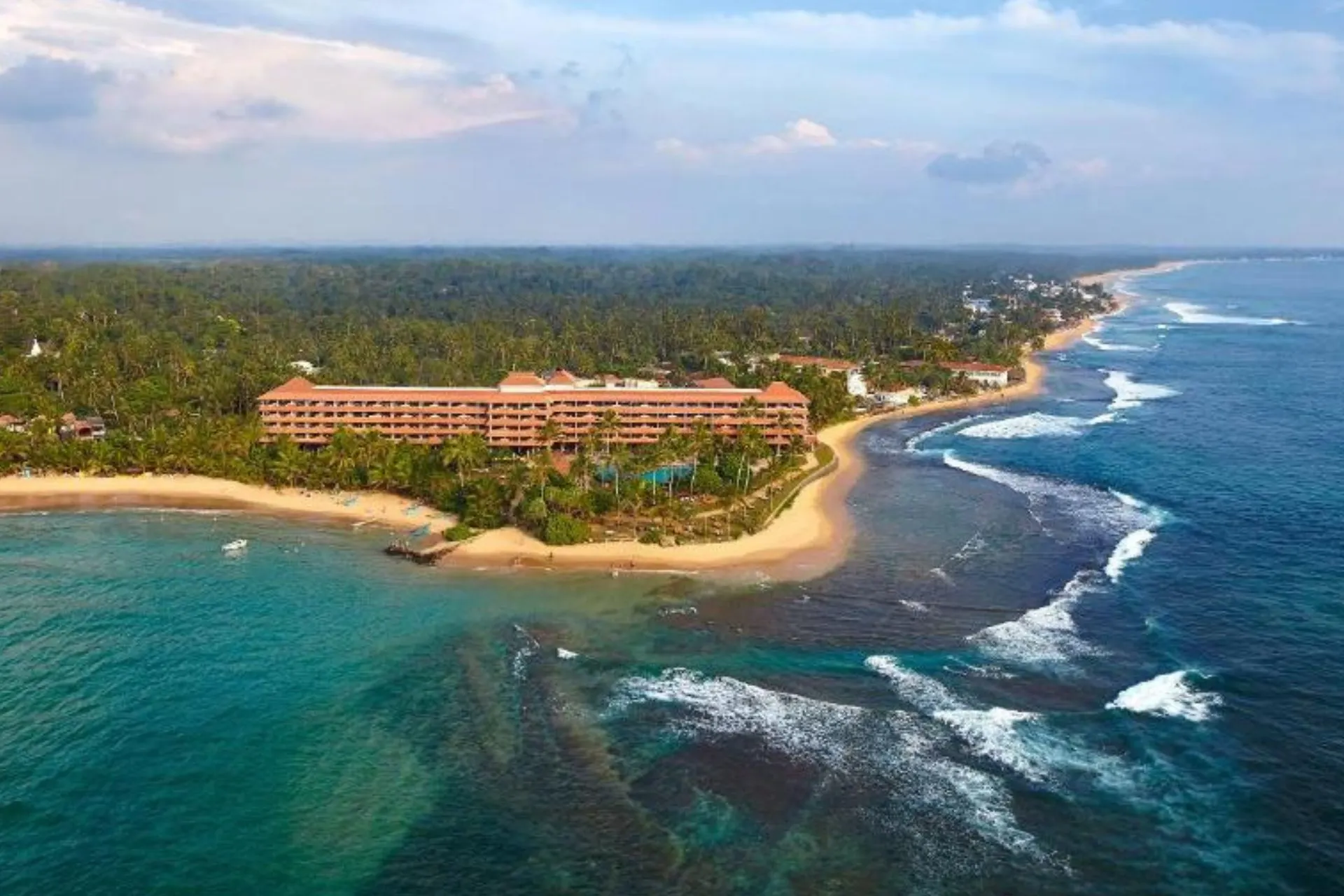 Luchtfoto van Hikka Tranz by Cinnamon langs de kust van Hikkaduwa, met langgerekt strand, weelderig groen en golvende oceaan tot aan de horizon.