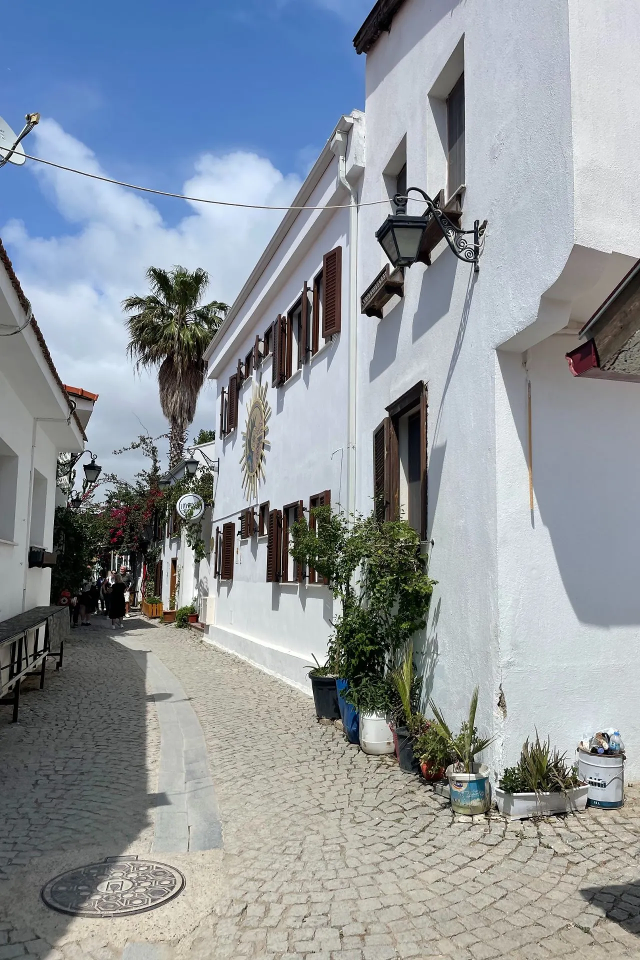 Wit straatje in Sığacık met charmante huizen, houten luiken, bloemen en een zonneschildering op de gevel.