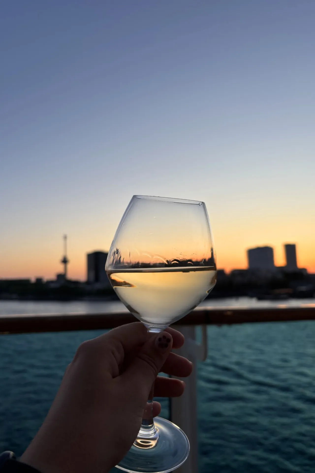 Glas witte wijn aan boord van de Costa Diadema met een kleurrijke zonsondergang op de achtergrond.
