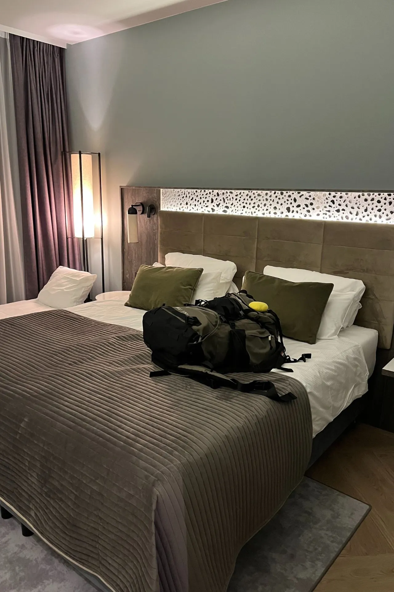 Een sfeervolle hotelkamer met een groot comfortabel bed, zachte verlichting en een backpack op het bed, klaar voor een avontuurlijke reis. Leonardo Royal Munich Hotel