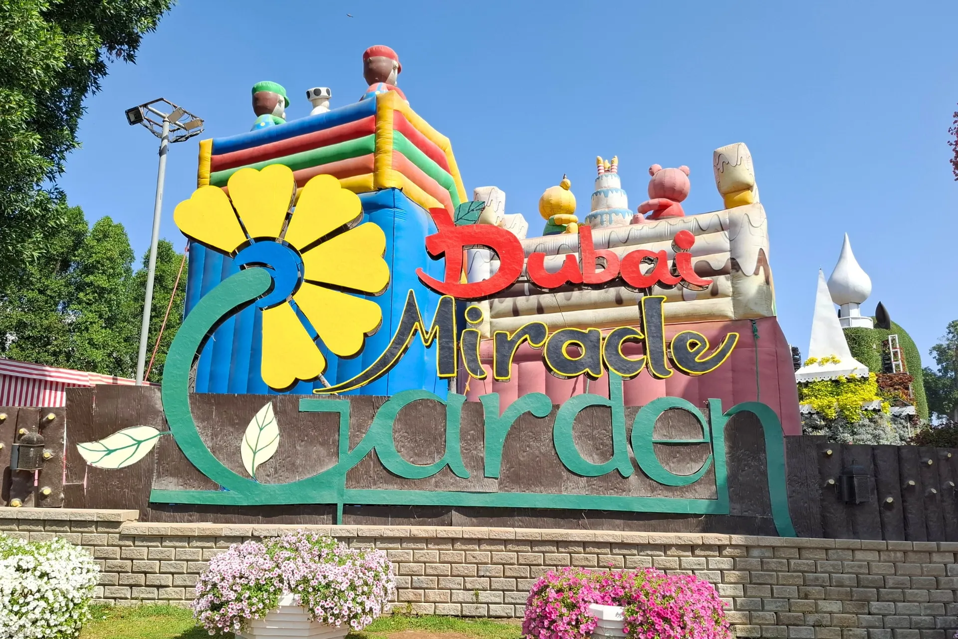 Kleurrijk entreebord bij Dubai Miracle Garden, met felle zonneschijn en een levendige sfeer.