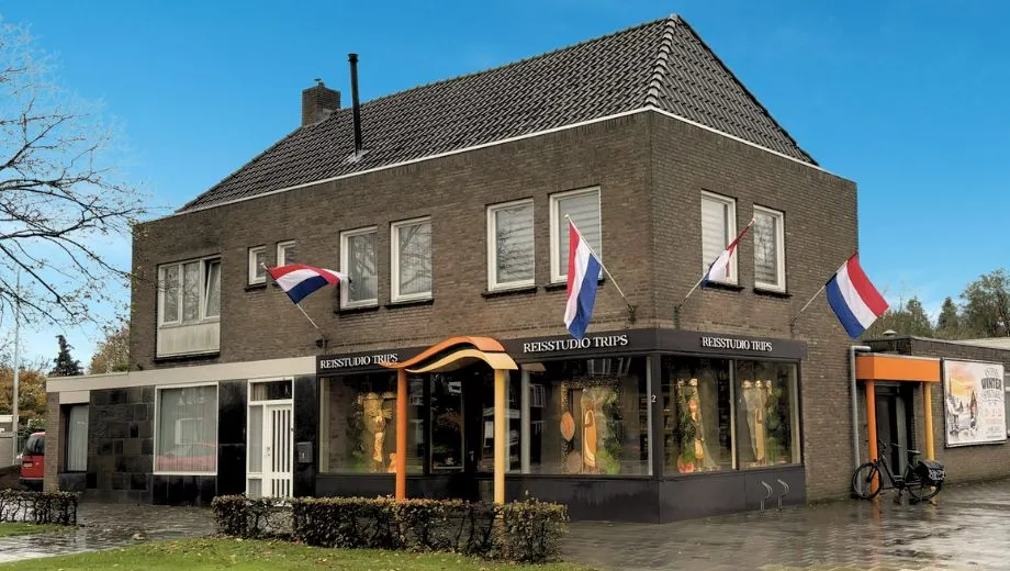 Reisbureau filiaal Asten van Travelcenter de Wit, oud gebouw en mooie blauwe lucht. Nederlandse vlag hangt uit.