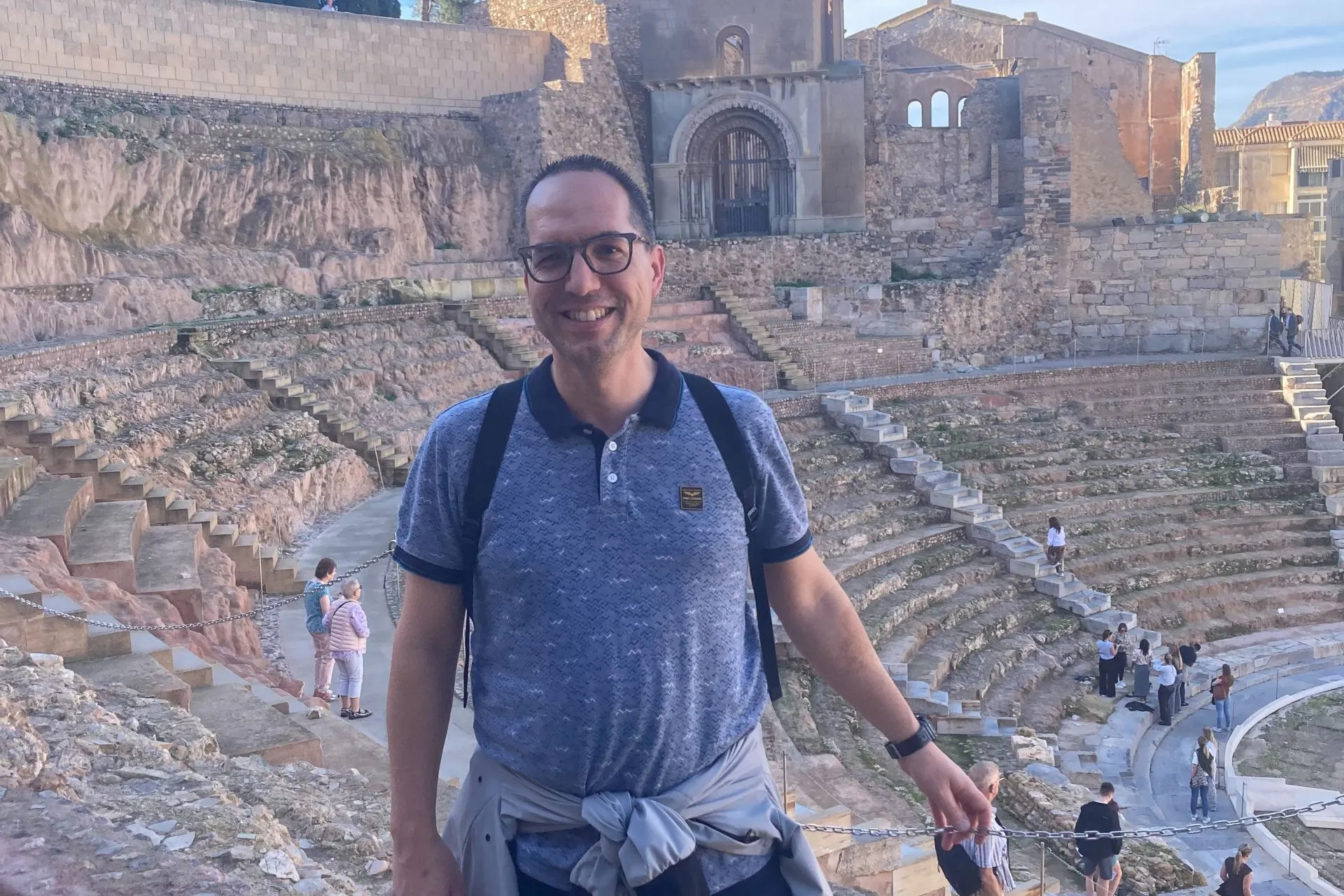 Reisadviseur Dino poseert voor een historische arena in Cartagena, Spanje, met stenen trappen en een oud gebouw op de achtergrond.
