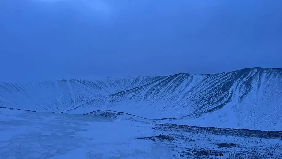 Winterse vulkaankrater Hverfjall in Noord‑IJsland, bedekt met sneeuw onder een blauwe hemel.
