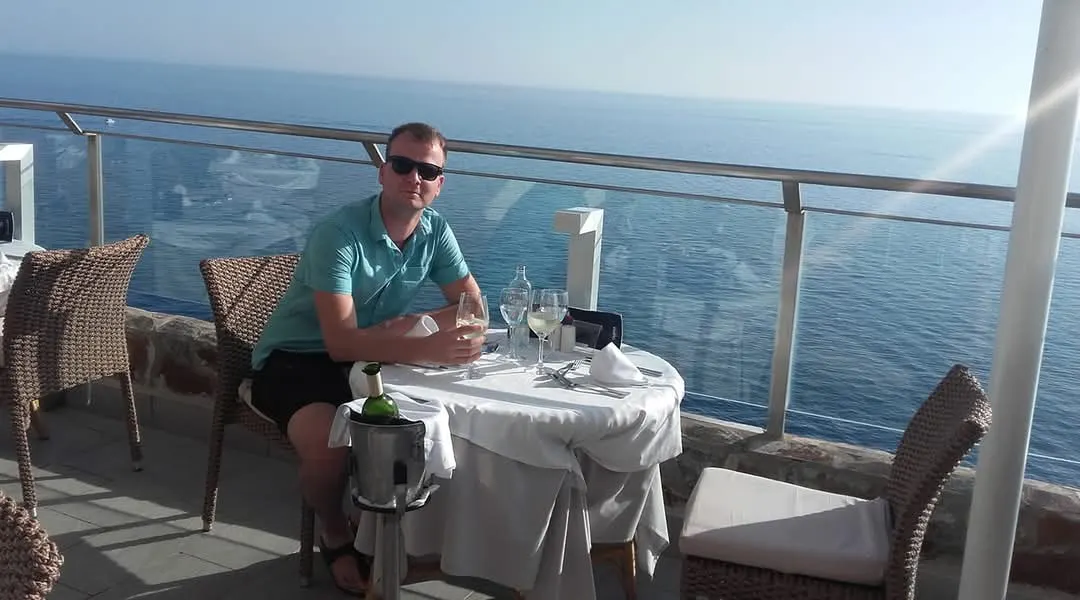 Leuke foto van een man met een zonnebril op een vissersboot aan een tafeltje met wit kleed en uitzicht op het water.