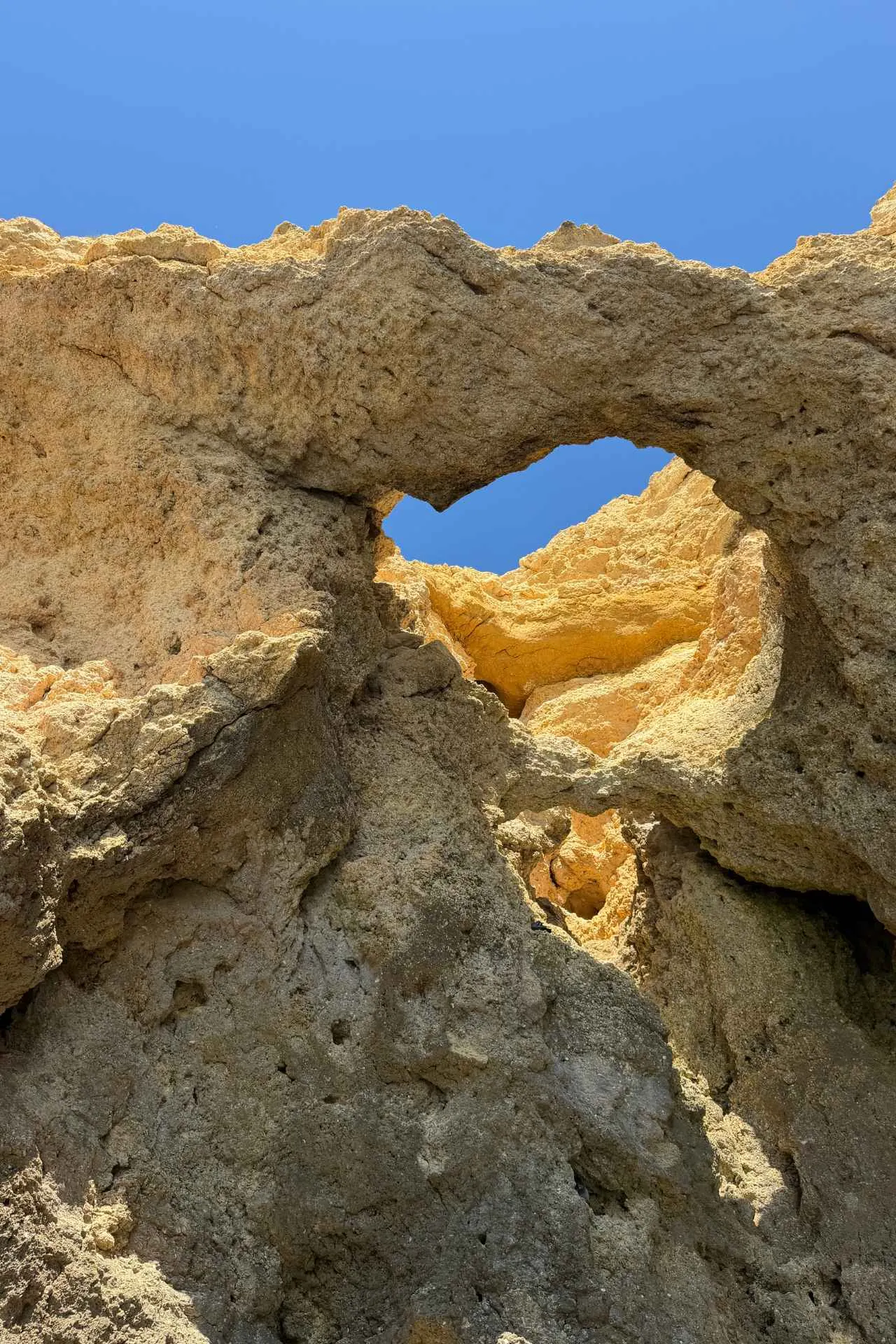 Bijzondere rotsformatie aan de kust van de Algarve met helderblauwe lucht op de achtergrond.