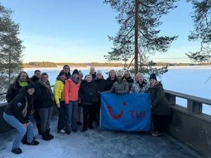 Foto van een groep mensen met een vlag van TUI, iedereen is warm aangekleed en je ziet een heldere blauwe lucht in Arctic lakeland Finland.