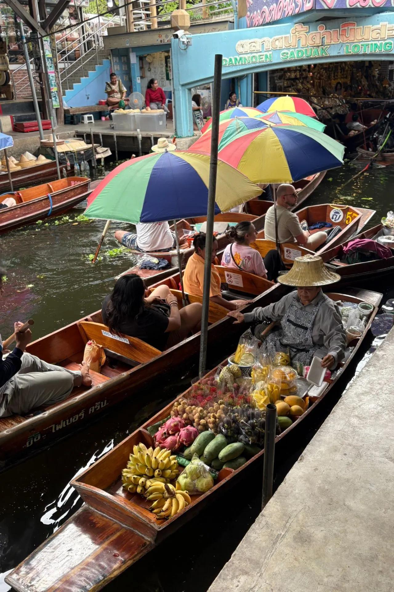 Groot kleurrijk standbeeld van de godin Guanyin met vele armen, elk met een symbolisch voorwerp, in een tempelcomplex onder een blauwe hemel.