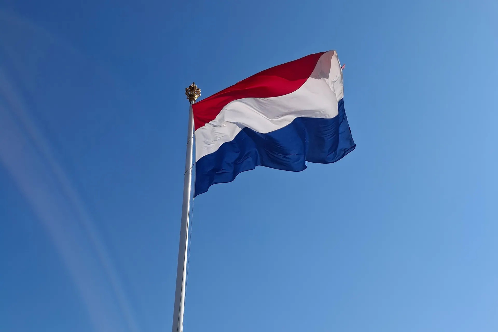 Nederlandse vlag wappert trots bij Paleis Het Loo tegen een lichte hemel.