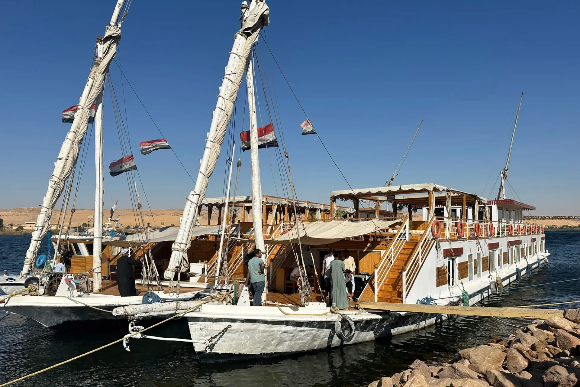 Grote Nijlcruiseboot in Egypte met wapperende Egyptische vlaggen aan dek, aangemeerd langs de oever.