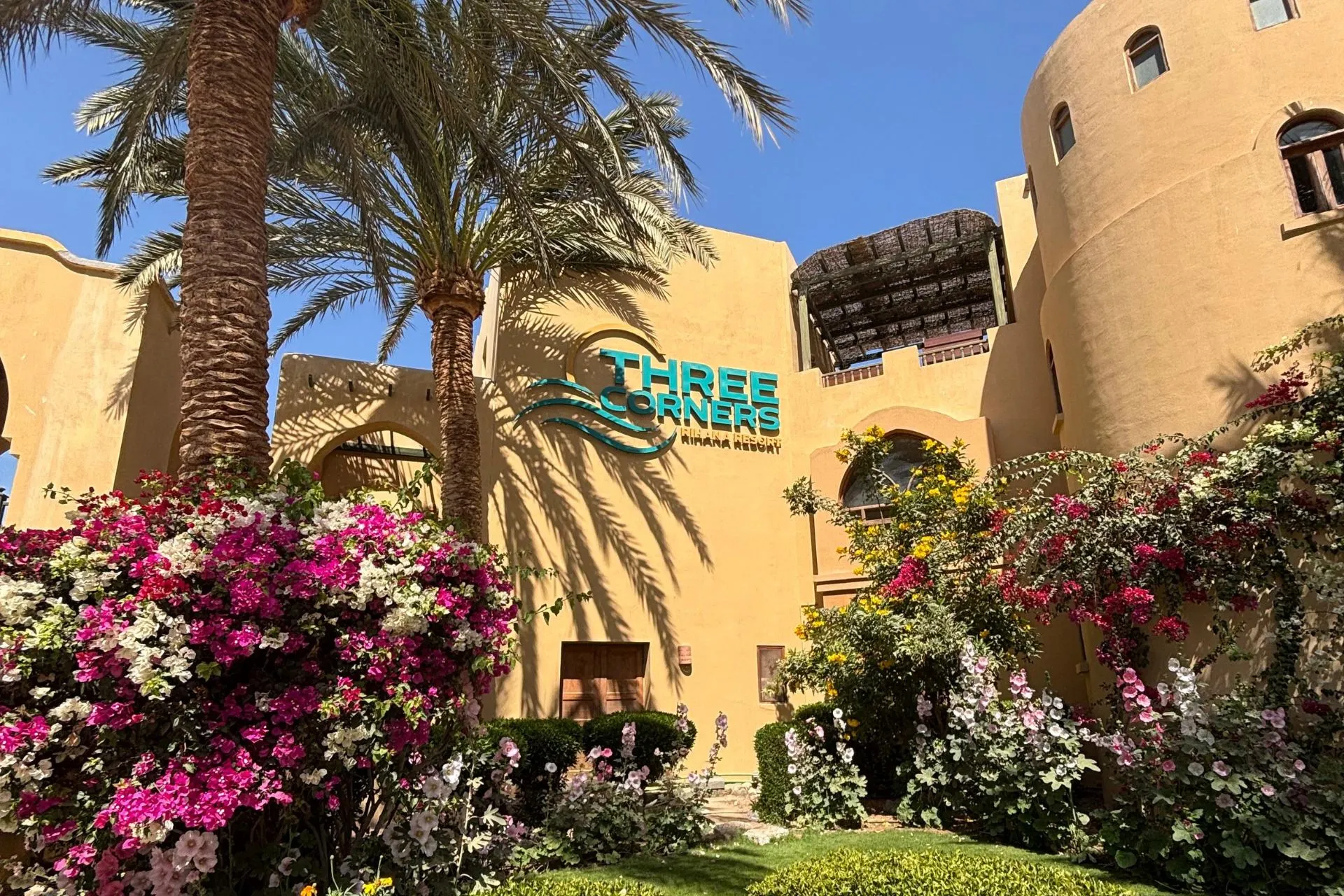 Entree van Three Corners Rihana Resort El Gouna met bloemen en palmbomen in Egypte