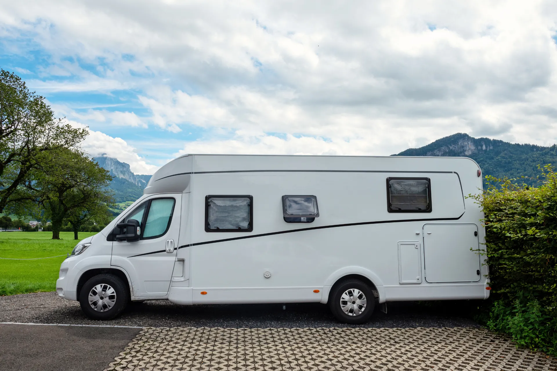 Witte camper geparkeerd op een parkeerplaats in Canada, met op de achtergrond bergen en veel groen.