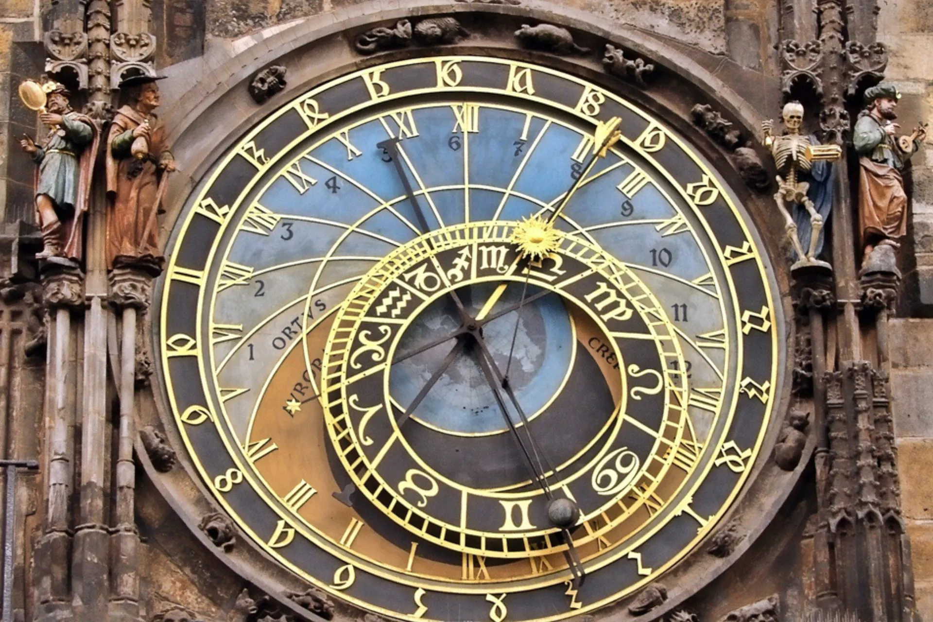 Detailfoto van de beroemde astronomische klok in Praag, ook bekend als het Orloj, gelegen aan het Oude Stadsplein. Het middeleeuwse uurwerk toont een complexe wijzerplaat met gouden cijfers, astrologische symbolen en een blauwe achtergrond, omringd door gedetailleerde beelden van heiligen. Een iconische toeristische attractie en historisch meesterwerk van gotische en astronomische kunst in Tsjechië.