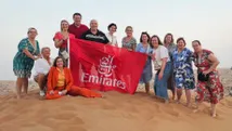 Groepsfoto van reisadviseurs met een rode Emirates-vlag, poseren in de duinen van Ras Al Khaimah.
