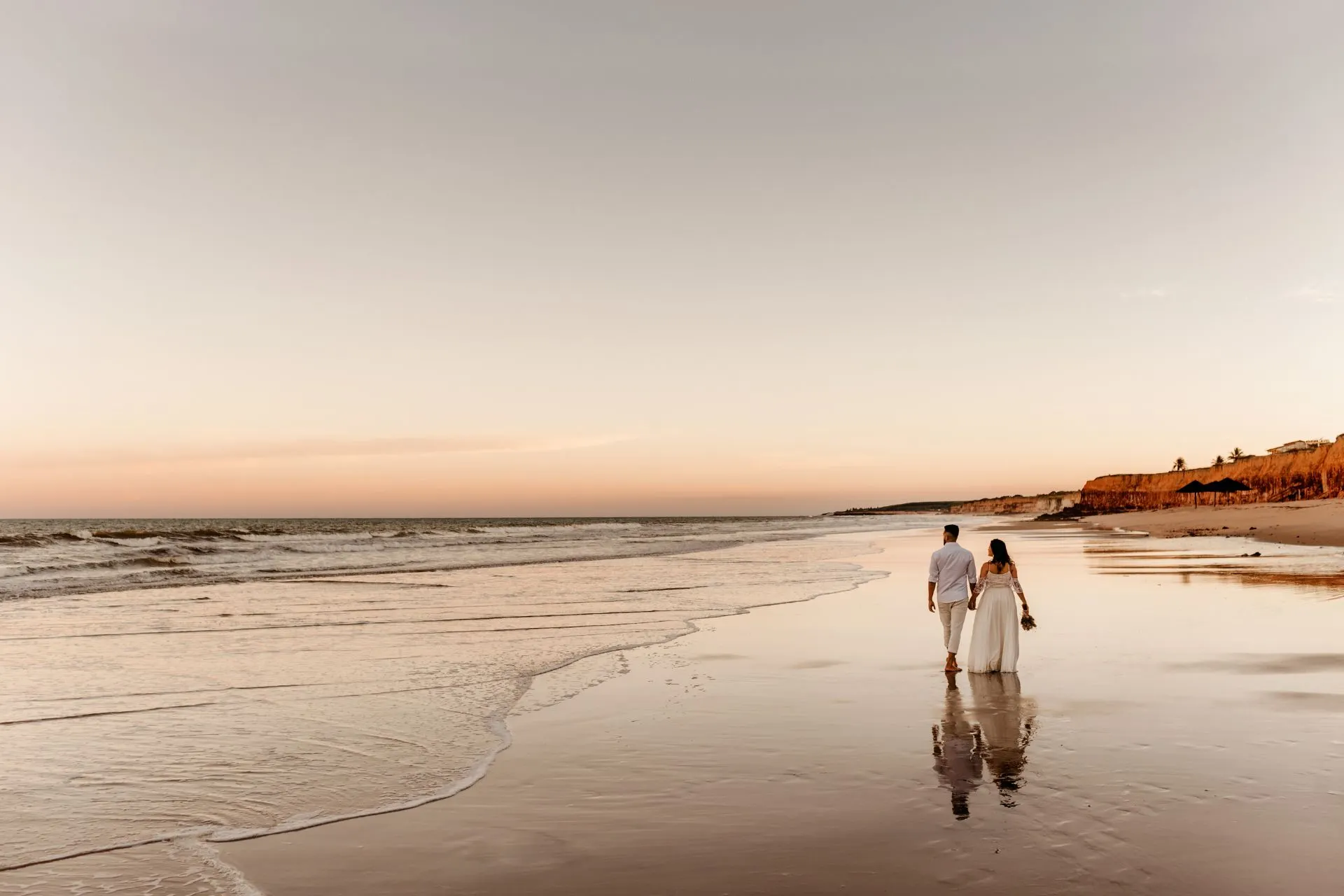 Een stel wandelt hand in hand langs het strand tijdens een adembenemende zonsondergang, omringd door de warme gloed van de ondergang van de zon, genietend van hun romantische moment.