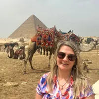 Naomi poseert lachend voor een piramide met een kameel op de achtergrond in Egypte.