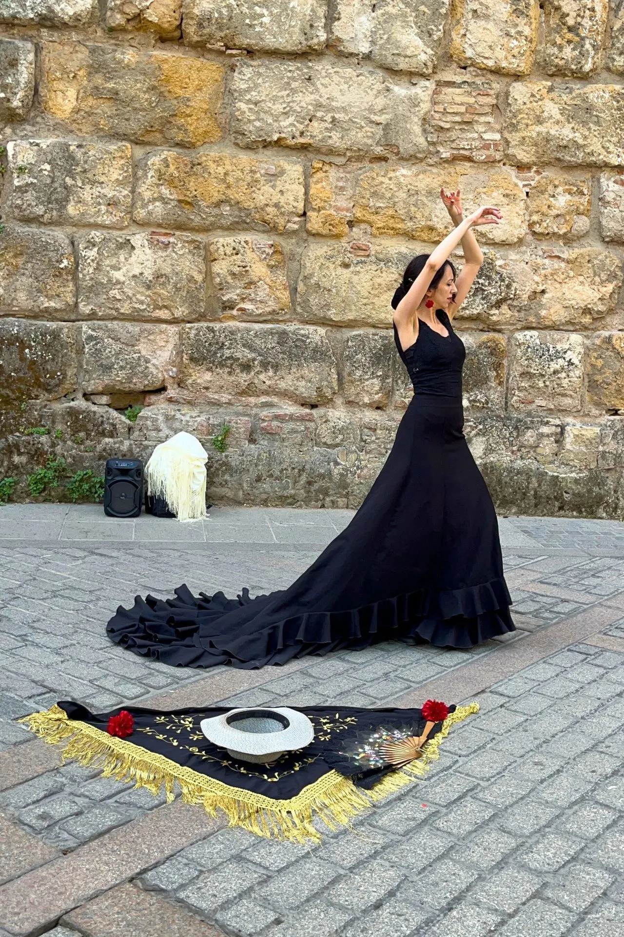 Flamencodanseres voert een expressieve dans uit op straat in Sevilla, Spanje. Ze draagt een lange zwarte jurk met sleep en rode oorbellen. Op de grond liggen een zwart sjaaltje met franjes, een Spaanse waaier en een hoed.