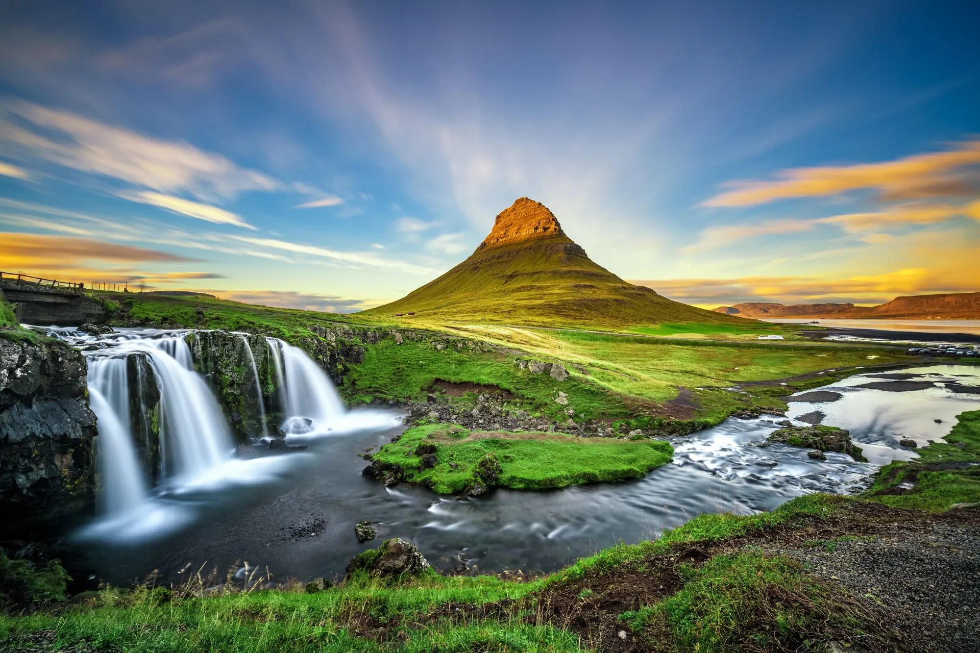 Het iconische Kirkjufell-gebergte in IJsland, met een waterval op de voorgrond en een kleurrijke lucht bij zonsondergang